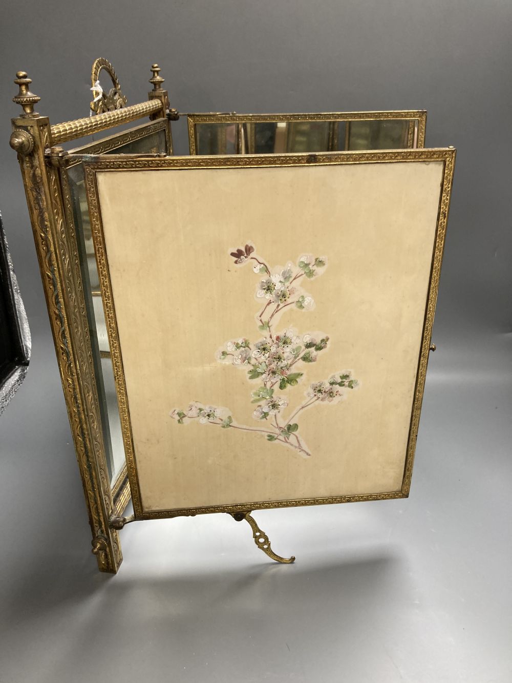 A gilt framed triptych mirror with faux ivory angelic panel and similar floral painted panel, height 41cm